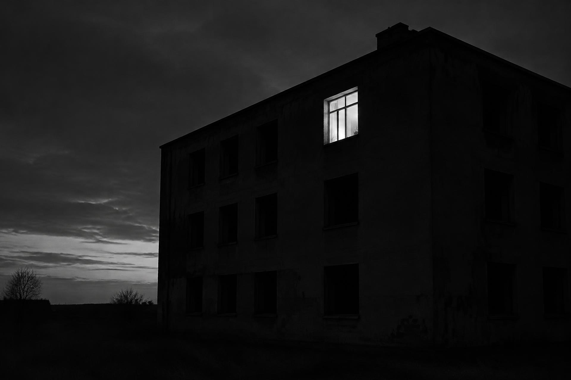 Einzelnes erleuchtetes Fenster in einem dunklen, leerstehenden Gebäude